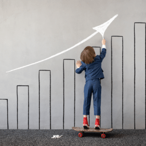 Kid wearing a suit on a skateboard pointing up at an arrow painted on the wall, showing the progression of child development