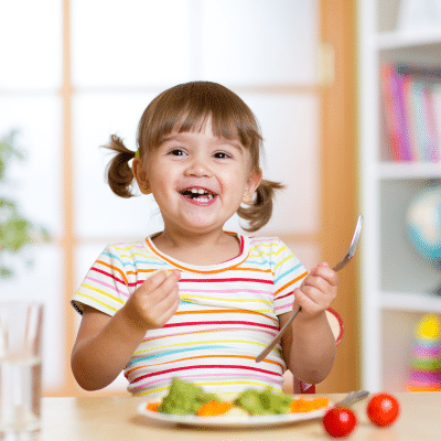 A child smiling at a plate of food, representing healthy eating for kids