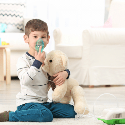 A boy holding a teddy bear and oxygen mask, representing childhood asthma treatment