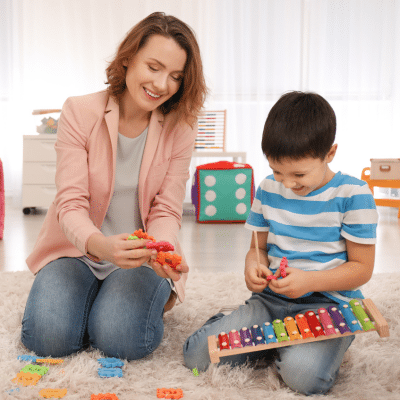 Woman working with a little boy in a play room, representing early signs of autism